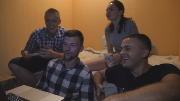 Grupo de pessoas assistindo filme de comédia ou vídeo engraçado de mídia social no laptop em casa. Homem feliz comer lanches enquanto procura programa de tv on-line no computador. Menina jovem acariciando gato sentado na cama — Vídeo de Stock