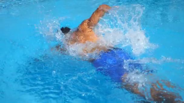 澄んだ青い水でプールを横切って浮かぶ認識できないスポーティな男。夏晴れた日にリゾートで泳いだり、レクリエーションを楽しむ若者。休暇や休日の概念。サイドビュー スローモーション — ストック動画