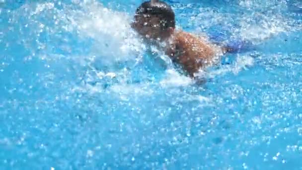 Hombre deportivo guapo flotando a través de la piscina con agua azul claro. Joven chico nadando y disfrutando de la recreación en el resort en verano día soleado. Concepto de vacaciones o vacaciones. Vista frontal Cámara lenta — Vídeo de stock
