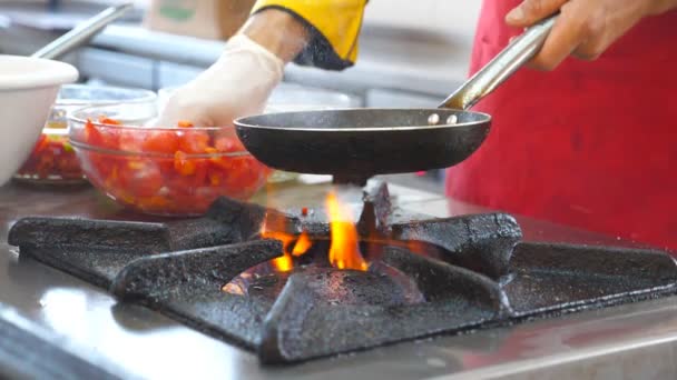 Unrecognizable chef cooking vegetarian dish in modern kitchen of restaurant. Male cook holding hot pan and throwing fresh vegetables into it. Cooking process in flambe style. Side view Slow motion — Stock Video