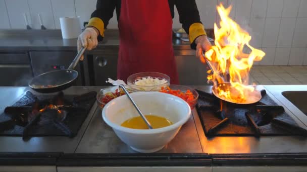 Felismerhetetlen séf gazdaság két serpenyő és főzési flambírozott stílus étel a modern konyha az étterem. Férfi szakács feldobás és sütés zöldségek skillets a tűzhely. Fogalma főzés. Elülső nézet SlowMo — Stock videók