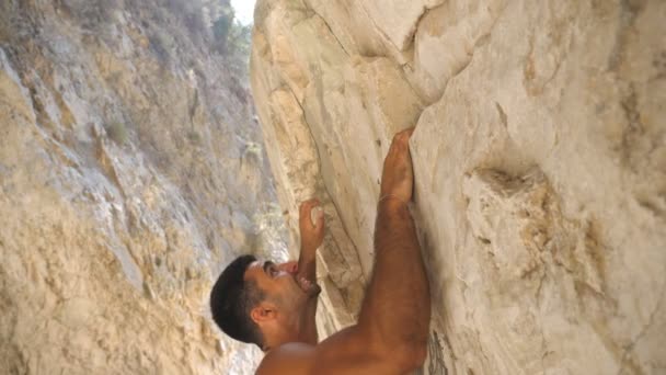 ロックでの若い筋肉の男の登山の側面図。岩のピークに上昇強い男は偉大な努力を作ります。山の頂上への道の登山。屋外の男性トレーニング。スローモーションのクローズアップ — ストック動画