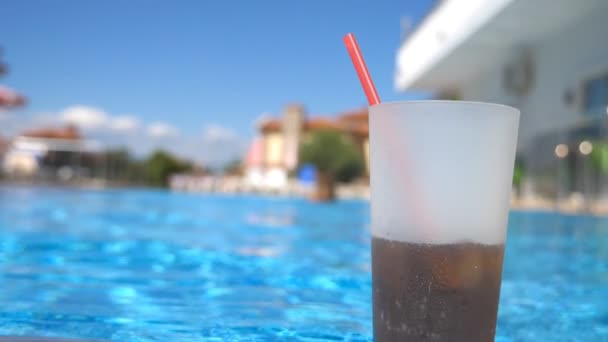 Close up de bebida refrescante com palha de pé perto da piscina vazia do hotel. Vista sobre cocktail frio no fundo da bacia. Movimento lento — Vídeo de Stock