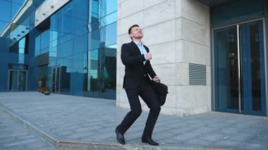 Caddenin üzerinde iyi bir anlaşma, takım elbiseli Genç mutlu işadamı sevinir. Başarılı ofis çalışanı evrak çantası ile modern building yakınındaki zafer dansı yapıyor. Yakışıklı adam başarı zevk. Ağır çekim