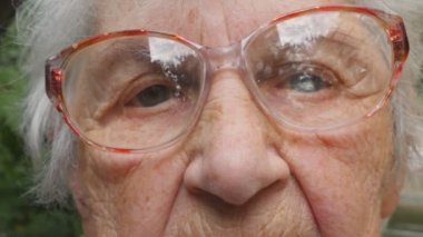 Gözlüklü yaşlı kadın kameraya bakıyor. Gözlüklü büyükanne dışarıda vakit geçiriyor. Üzgün büyükanne nin dış mekanportresi. Yavaş hareketi kapat