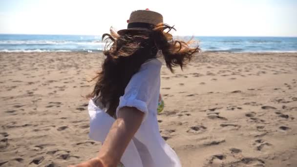 Girl holding male hand and running on beach to the ocean. Follow me shot of young woman in hat pull her boyfriend on the sea shore. Summer vacation or holiday concept. Point of view POV Slow motion — Stock Video