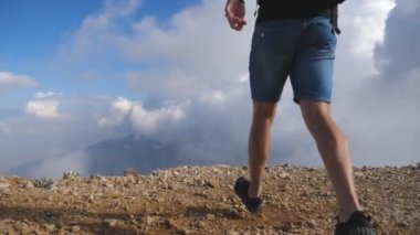 Sırt çantası ile genç erkek yürüyüşçü arka planda bulutlu gökyüzü ile dağın tepesine ulaşan ve el kaldırarak. Boy turist tepenin kenarında duran ve muzaffer silah uzanan. Yavaş çekim