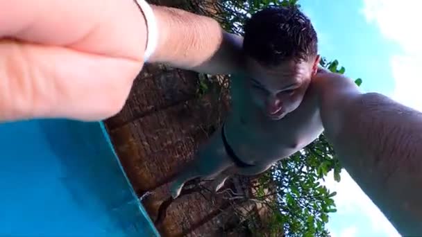 Νέος άνθρωπος άλμα στην πισίνα με την κάμερα δράσης στο χέρι. Καυκάσιος τύπος που κολυμπάει κάτω από νερό σε λεκάνη την ηλιόλουστη μέρα. Ένα αγόρι που χαλαρώνει τις καλοκαιρινές διακοπές. Υποβρύχια πλάνα. Αργή κίνηση close up — Αρχείο Βίντεο