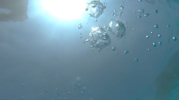Множество маленьких пузырьков воздуха, поднимающихся в бирюзовом чистом море. Теплый солнечный свет проникает в кристально чистую океанскую воду в солнечный летний день. Пузырьки воздуха всплывают на поверхность воды. Медленное движение — стоковое видео