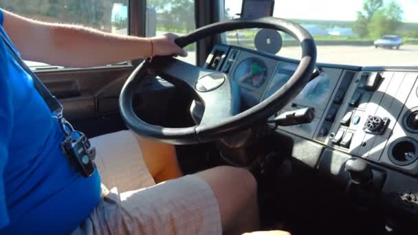 Nierozpoznawalny kierowca siedzi za kierownicą swojej ciężarówki jazdy na drodze wiejskiej w słoneczny dzień. Człowiek kontrolujący ciężarówki jazdy do celu. Widok wewnątrz kabiny ciężarówki. Zbliżenie zwolnionym tempie — Wideo stockowe