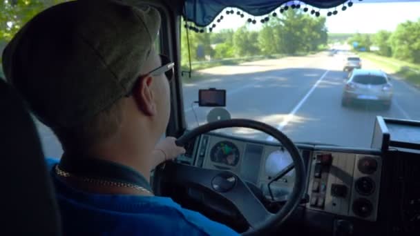 晴れた日に郡の道路に乗って認識できないローリードライバー。キャップとサングラスをかけた男がトラックの注意深い見守り道をコントロールしている。キャビン内からのトラフィックのビュー。インサイドショットスローモクローズアップ — ストック動画