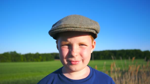 Πορτρέτο του ευτυχισμένο αγόρι στέκεται στο αγροτικό περιβάλλον και γελώντας καλύπτοντας το πρόσωπό του με το χέρι. Αξιολάτρευτο όμορφο μωρό κοιτάζοντας την κάμερα με χαρούμενο χαμόγελο. Κλείστε τα συναισθήματα του αρσενικού παιδιού. Αργή κίνηση — Αρχείο Βίντεο