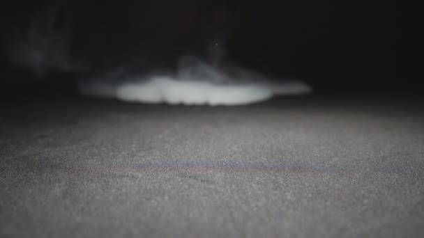 Gros plan d'un club de vapeur de lait expirant d'une cigarette électronique ou d'un narguilé à la surface du sol. Bouche masculine soufflant de la fumée pure blanche du singe. Fond noir. Vue basse Mouvement lent — Video