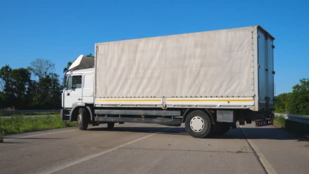 Vista lateral en camión blanco con remolque de carga girando en medio de la carretera. Conductor de camiones transportando mercancías en su vehículo. Transporte y concepto logístico. Movimiento lento — Vídeo de stock