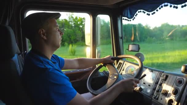 Profil av lastbilschaufför rida genom landsbygden på kvällen. Man i hatten kontrollera sin lastbil och njuter resa. Utsikt inne i bil stugan. Transport av logistikkoncept. Slow motion närbild — Stockvideo