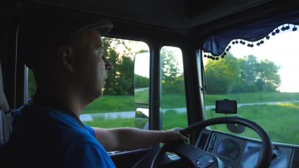 Profil člověka projížděného krajinou s nádherným západem slunce na pozadí. Řidič náklaďáku řídí jeho náklaďák autem do místa určení. Dopravní a logistická koncepce. Pohled do kabiny nákladních aut. Zpomalit na mo