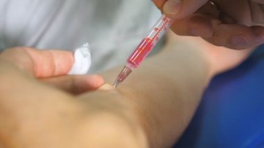Hastanedeki hastanın derisine şırınga ile aşı yapan bir doktorun erkek ellerine yakın çekim. Klinikteki genç hasta adamın koluna iğne batırılmış. Sağlık ve Tıp Konsepti