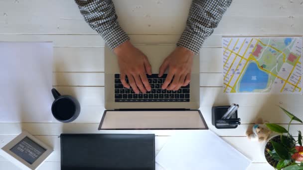 Mužská ruka při psaní textu na klávesnici laptopu na bílém dřevěném stole. Podnikatel používá notebook pro svou práci. Nejvyšší pohled na pracoviště zaměstnance kanceláře s jeho osobními věcmi. Nad střelou pomalý mo zavřít — Stock video