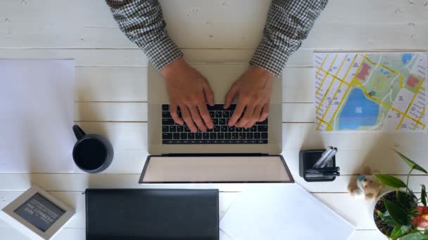 Manliga händer skriva text på laptop tangentbord på vit trä skrivbord. Affärsman med anteckningsbok för sitt arbete. Top syn på arbetsplatsen för kontorspersonal med sina personliga saker. Ovan skott långsam Mo närbild — Stockvideo