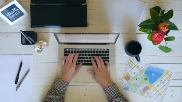 Brazos masculinos escribiendo texto en el teclado del ordenador portátil en el escritorio de madera blanca. Empresario tomando bolígrafo y tomando notas en documento. Vista superior en el lugar de trabajo del empleado de oficina con sus cosas personales. Lento mo Primer plano — Vídeos de Stock