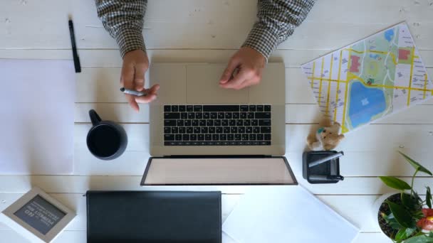 Mężczyzna trzyma długopis i kręci go w ręku. Biznesmen surfing Internet na laptopie. Facet pracuje nad swoim miejscem pracy w biurze Loft. Powyżej strzał powolny ruch zbliżenie — Wideo stockowe