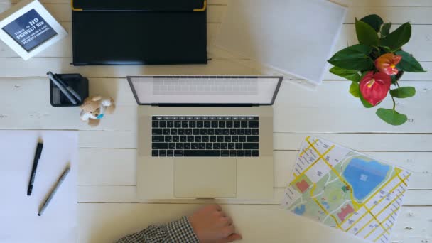 Невпізнаваний чоловік п'є каву і продовжує працювати над проектом. Чоловічі руки друкують текст на клавіатурі ноутбука на білому дерев'яному столі. Вид зверху на робоче місце творчого офісного працівника. Повільний mo Крупним планом — стокове відео