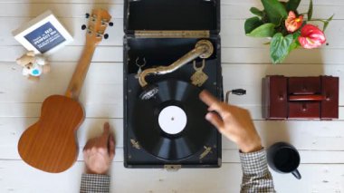 Beyaz masada vintage gramofon üzerinde dönen vinil kayıt yakın. Klasik müzikten zevk gösteren erkek ellerinin en iyi görünümü. Tanınmayan bir adam dinliyor ve kayıttan zevk alıyor. Yavaş çekim