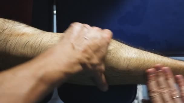 Las manos masculinas del masajista haciendo lentamente frotar el pie del joven deportista en el salón. Los brazos del masajista profesional que cura el masaje de la pierna del atleta acostado sobre la mesa de masaje en el salón. POV cámara lenta — Vídeo de stock
