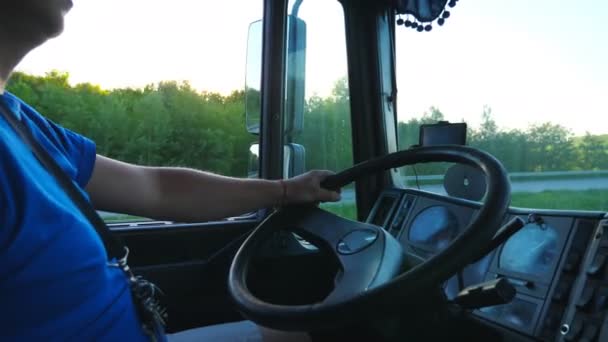 Řidič náklaďáku projížděli krajinou v době západu slunce. Muž, který ovládá jeho náklaďák, jede do cíle. Uzavřete volant a palubní desku auta. Pohled do kabiny nákladních aut. Boční zobrazení pomalý pohyb — Stock video