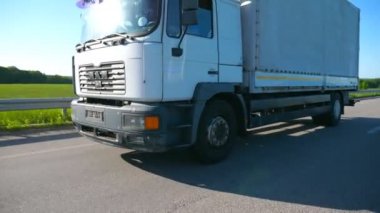 Kamera, karayolu üzerinde sürüş ve yaz gününde mal taşıma kargo römork ile kamyon izler. Kamyon arka planda güzel manzara ile ülke üzerinden sürme. Slow mo Yan görünüm Kapat