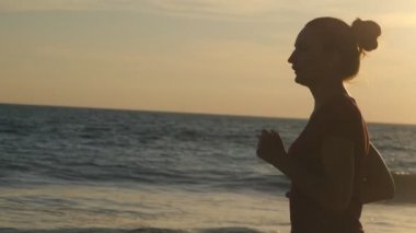 Güneş doğarken okyanus kıyısında koşan bir kız. Gün batımında sahilde koşan genç bir kadının silueti. Dişi sporcu dışarıda egzersiz yapıyor. Doğada sağlıklı, aktif bir yaşam tarzı. Yavaş çekim