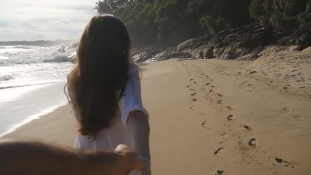 Sígueme la foto de una mujer joven tirando de su novio en la orilla del mar. Chica sosteniendo la mano masculina y corriendo en la playa tropical exótica al océano. Vacaciones de verano o vacaciones. Punto de vista. POV cámara lenta — Vídeos de Stock