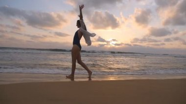 Mutlu kadın yürüyüş ve iplik sahilde okyanus yakın. Genç güzel kız hayattan zevk ve deniz sahilinde eğleniyor. Yaz tatili ya da tatil. Arka plan, günbatımı manzara. Ağır çekim