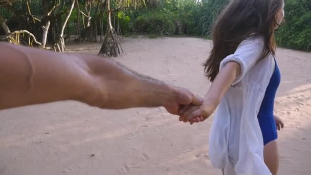 Vakker jente som holder mannlig hånd og løper på en tropisk eksotisk strand. Følg meg. Bilde av en ung kvinne. Dra kjæresten hennes på land. Sommerferie eller ferie. Synspunkt POV Langsom bevegelse – stockvideo