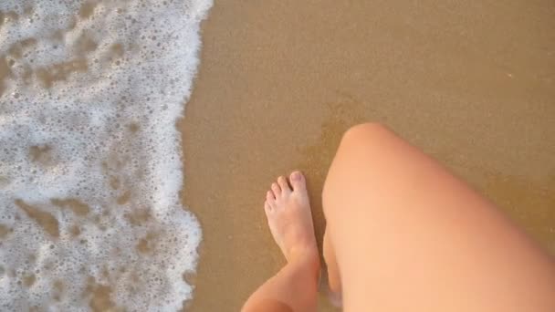 Sicht einer jungen Frau, die am goldenen Sand am Strand des Meeres tritt. weibliche Beine, die in der Nähe des Ozeans gehen. Barfuß eines Mädchens, das an sandigem Ufer mit Wellen geht. Sommerurlaub oder Urlaub Zeitlupe Nahaufnahme — Stockvideo