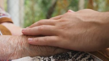 Genç erkek ve kırışık eller rahatlatıcı ve açık havada birbirlerini okşayarak. Torunu ve büyükanne dışarıda birlikte vakit geçiriyorlar. Sevecen ve sevgi dolu bir kavram. Yukarı yakın Yan görünüm Yavaş çekim