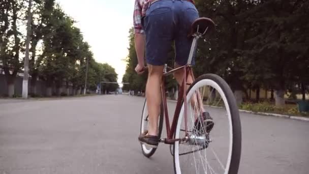 年轻人在公园路上骑着老式自行车。一个矮胖的家伙在户外骑车。健康积极的生活方式。低视角闭合慢动作 — 图库视频影像