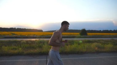 Ülkede yol günbatımında koşu kas delikanlı. Erkek koşucu için maratona profil açık çalıştırın. Mavi gökyüzü güneş ile karşı egzersiz atlet. Spor ve aktif yaşam tarzı. Ağır çekim