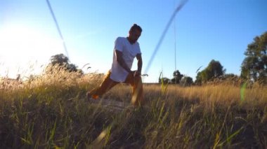 Güneşli bir günde çayırda egzersiz yapan genç adam. Sportif adam sahada minye yoga. Arka planda yaz manzarası. Sağlıklı aktif yaşam tarzı kavramı. Yakın çekim