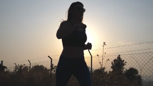 Seguindo para jogging menina desportiva na estrada do campo ao nascer do sol. Jovem a correr ao ar livre de manhã. Estilo de vida ativo saudável. Movimento lento — Vídeo de Stock