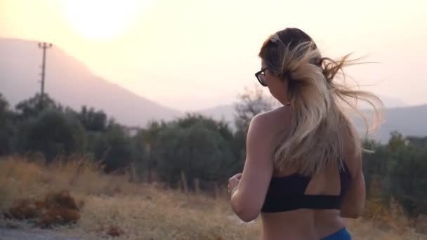 Mujer joven entrenando para correr maratón al aire libre. Chica deportiva corriendo en la carretera del campo. Vida activa saludable. Vista trasera trasera en cámara lenta — Vídeos de Stock