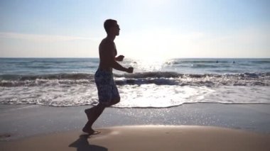 Deniz sahilde sabah koşan genç sportif adam. Sahil boyunca güneşli bir günde koşu atletik bir adam. Açık egzersiz erkek sporcu. Sağlıklı aktif yaşam tarzı. Yan görünümü ağır çekim