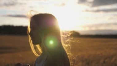 Gün batımında arpa tarlasının bulanık arka planına atlayan neşeli gülümseyen kızın yakın çekim. Güneş ışığı arka plan ile buğday çayırda eğlenmek sarı saçlı mutlu gülen çocuk. Yavaş mo