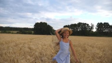 Arpa çayır üzerinde koşu hasır şapka sevimli mutlu çocuk. Uzun sarı saçlı güzel kız buğday tarlasında koşuyor. Küçük gülümseyen çocuk altın çiftlikte vakit geçiriyor. Yavaş çekim