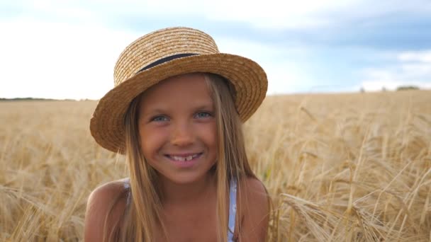 Retrato de criança feliz rindo com cabelo loiro no prado de trigo. Menina sorridente bonita em chapéu de palha olhando para a câmera contra o fundo do campo de cevada na fazenda orgânica. Fechar — Vídeo de Stock