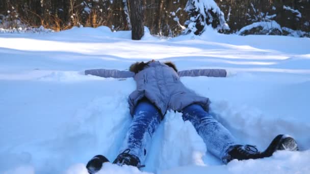 Unrecognizable young girl lying on snowy meadow and making angel. Happy woman playing in snow enjoying winter time. Cheerful lady having fun outdoor. Concept of winter holiday. Slow motion Close up — Stock Video