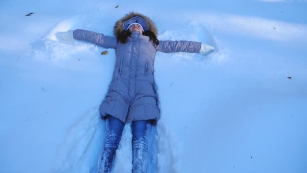 Rapariga deitada no prado nevado e fazendo anjo. Mulher feliz brincando na neve aproveitando o inverno. Senhora alegre se divertindo ao ar livre. Conceito de férias de inverno. Lento movimento Fechar — Vídeo de Stock