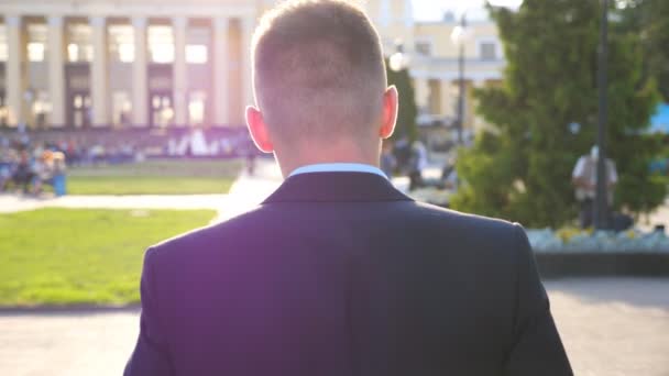 Unerkennbarer Geschäftsmann, der bei sonnigem Wetter durch die Stadt spaziert. Mann, der auf dem Weg zur Arbeit durch die Straße schlendert. erfolgreicher Manager, der frühmorgens zur Arbeit geht. Zeitlupe — Stockvideo