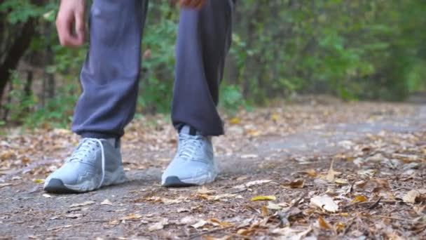 Nahaufnahme eines starken Mannes, der im Frühherbstwald auf einem Pfad joggt. Sportler bindet beim Training im Freien Schnürsenkel an Turnschuhe. Männliche Hände junger Sportler binden Schuhe an die Natur. niedrige Sicht — Stockvideo
