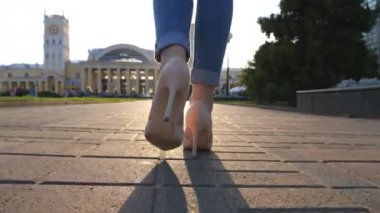 Yüksek topuklu ayakkabılı kadın bacakları şehir caddesinde yürüyor. Kendine güvenen bir kız gün batımında arka planda yürüyordu. Şehir ortamında gezinen tanınmayan bir kadın. Yavaş çekim